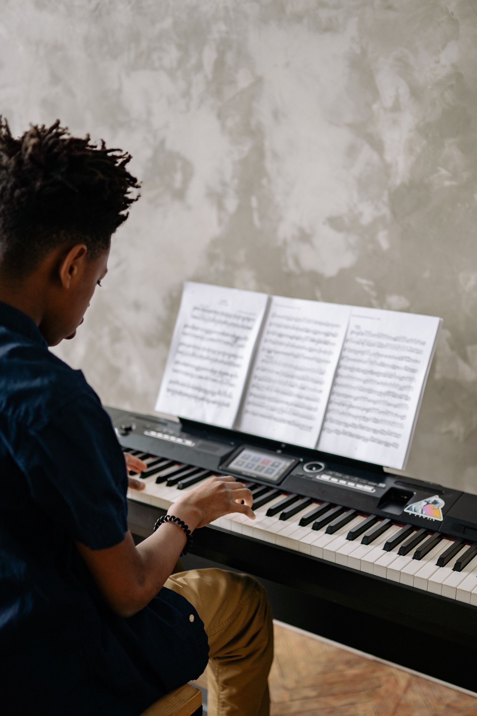 En ung pianist øver sig ved et keyboard med åbne noder foran sig.