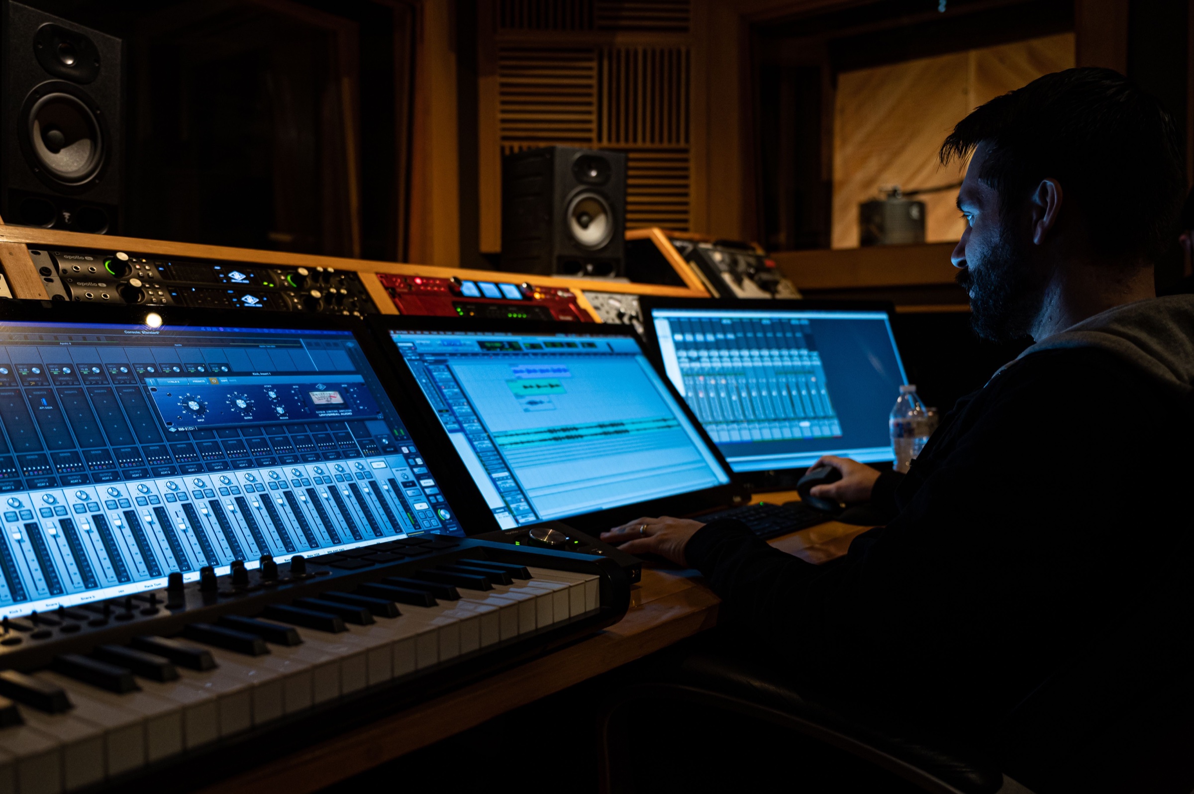En musikskaber arbejder ved keyboards, computere og digital lydsoftware i et professionelt studie.